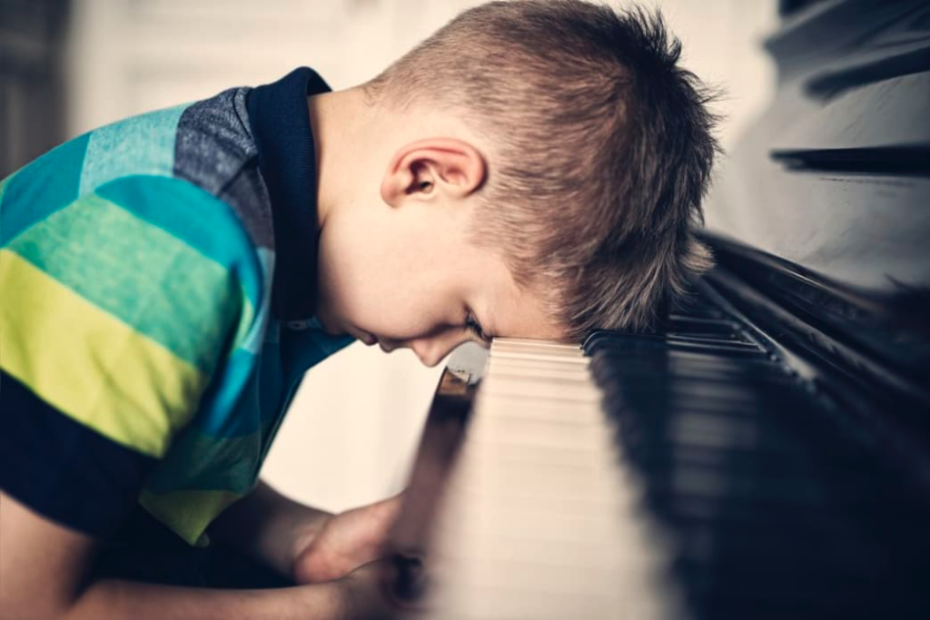 Child with head on piano keys. 