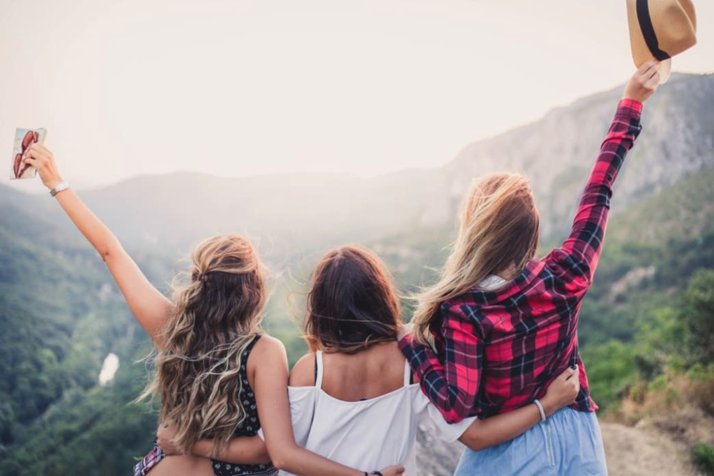 Three young women standing arm-in-arm overlooking mountains. 