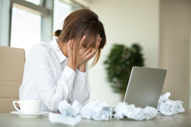 Stressed female worker feel despair surrounded by crumpled paper not able to write business letter or email, tired upset businesswoman have no motivation at work, suffering from headache or fatigue