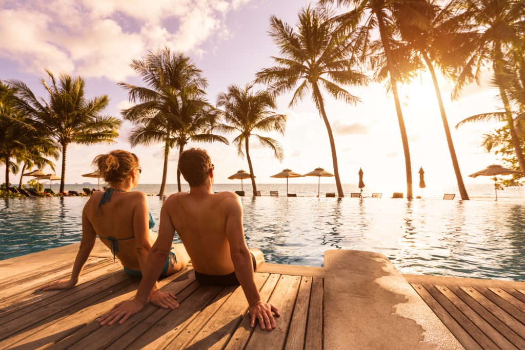 Couple enjoying beach vacation holidays at tropical resort with swimming pool and coconut palm trees near the coast with beautiful landscape at sunset, honeymoon destinationTake time to relax. 