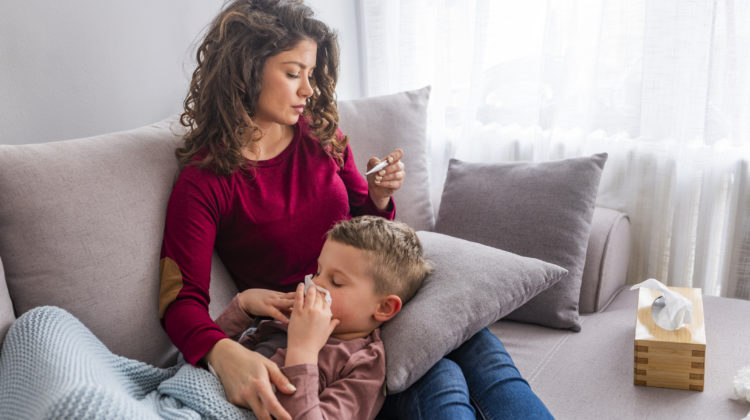 Close up of a mother checking the temperature of her boy with a thermometer on a couch in the living room at home. Mother take care of sickness little boy on the bed