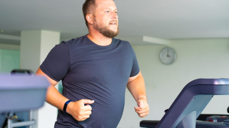 chubby man walking on running track, warming up on gym treadmill - testosterone levels and exercise 
