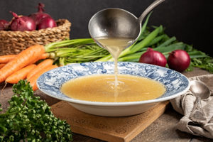 Bone Broth in a blue bowl.  A ladle is pouring more into the bowl. 