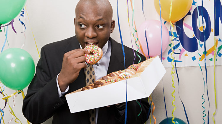 Man eating a donut at an office party - Those office party temptations don't have to sabotage your health goals.  - New Year's Resolutions
