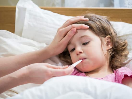 Sick young girl in bed with someone taking her temperature with a thermometer. 