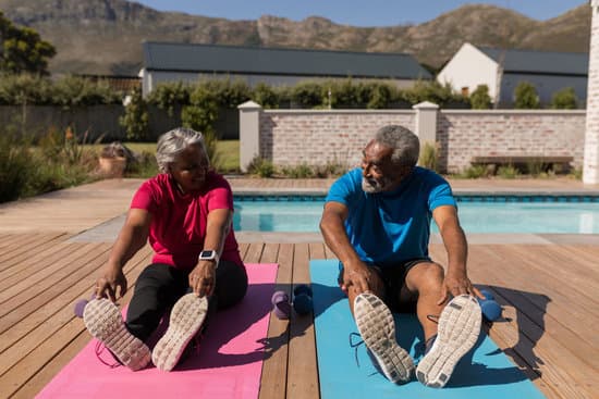 Senior woman and man stretching next to their pool on yoga mats. 