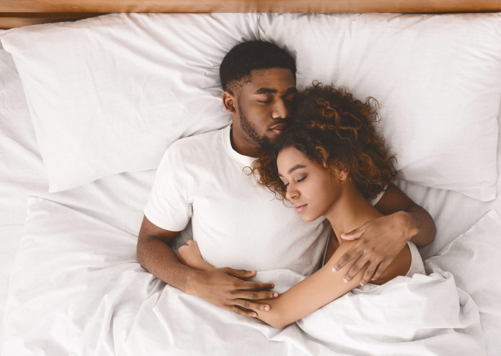 Lovely black couple lying in white bed, sleeping together, top view