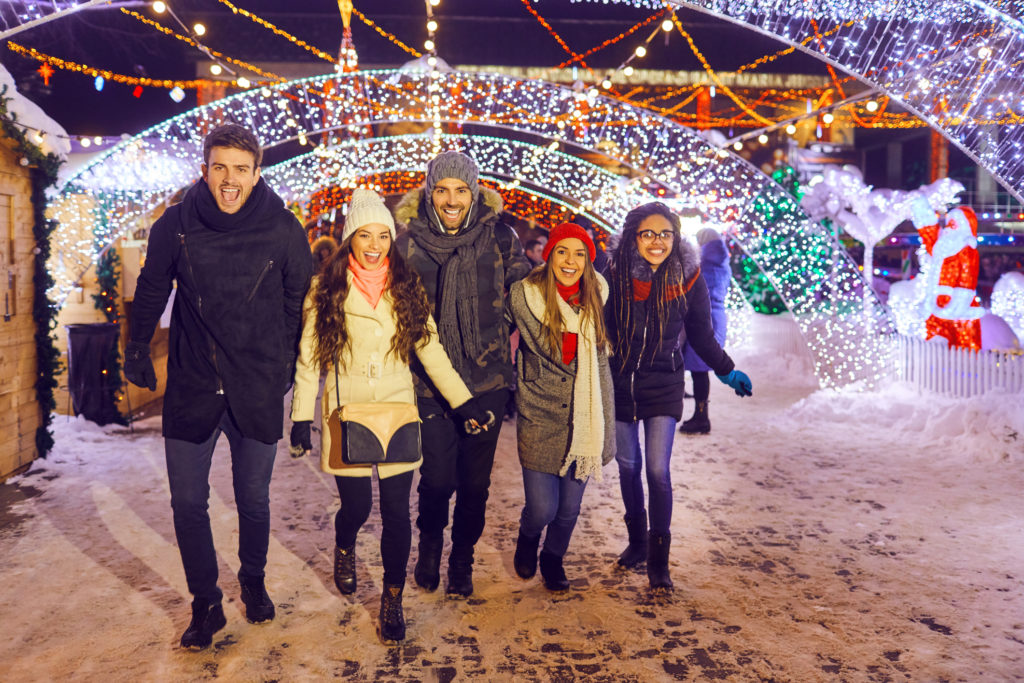 A group of friends have fun walking on Christmas streets at night. Touring lights with friends to help stick to your healthy holiday eating habits. 