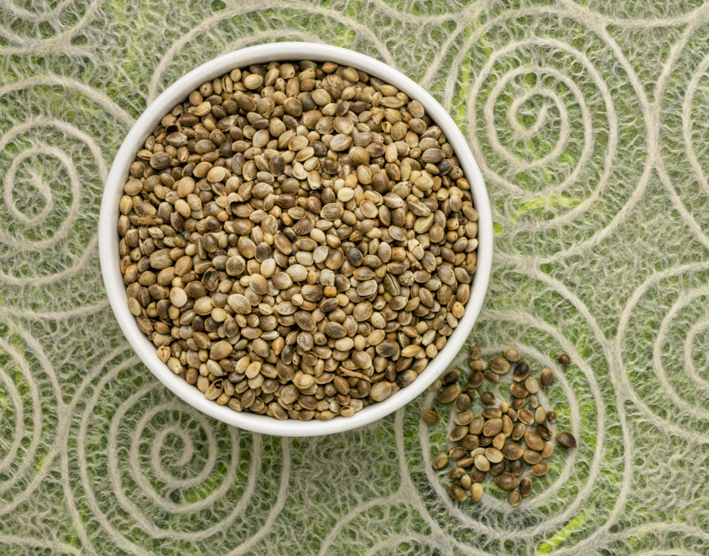 dry hemp seeds in a small ceramic bowl, top view against lace paper with spiral pattern