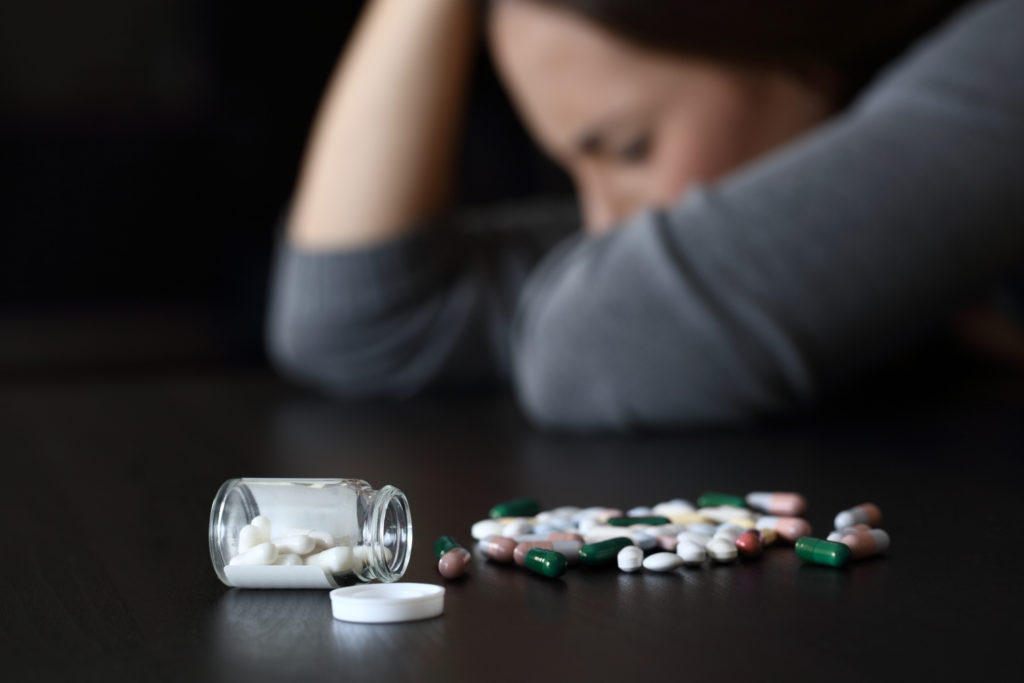 Close up of a depressed woman beside a lot of pills on a table on a dark background