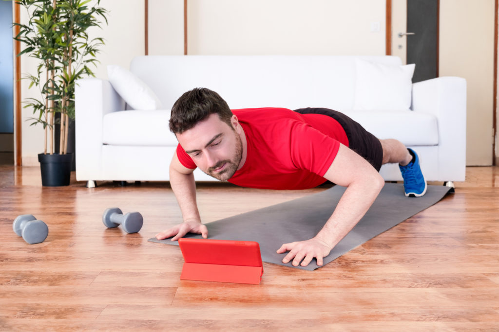 Man doing push ups at home watching digital tablet