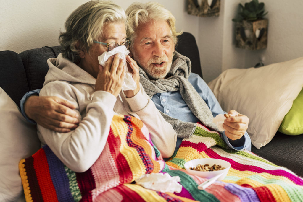 Couple of old aged senior people at home with seasonal winter cold illness disease  sit down on the sof together forever - health problems for retired man and woman with white hair