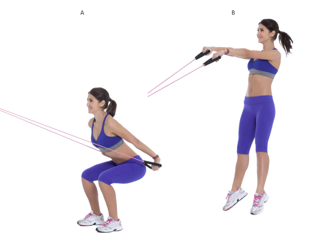 Holding onto the straps, squat all of the way down, getting your bum as close to the floor as possible. (A) When you reach the bottom of the squat, power upwards, jumping as high as you can, with your feet leaving the floor. (B)