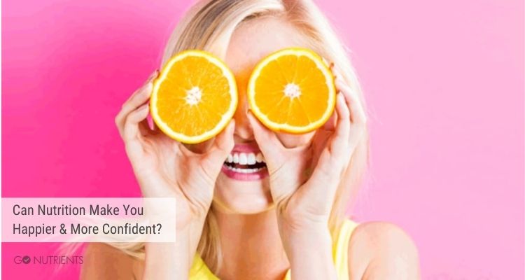 Can nutrition make you happier and more confident?  Photo:  Blond woman holding two slices of an orange over her eyes.  She has a big smile as well. 
