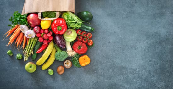 Fruits and vegetables spilling out a paper grocery bag. 