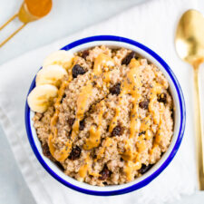 A bowl with the quinoa breakfast prepared and a gold spoon next to the bowl.  It is also garnished with slices of banana. 