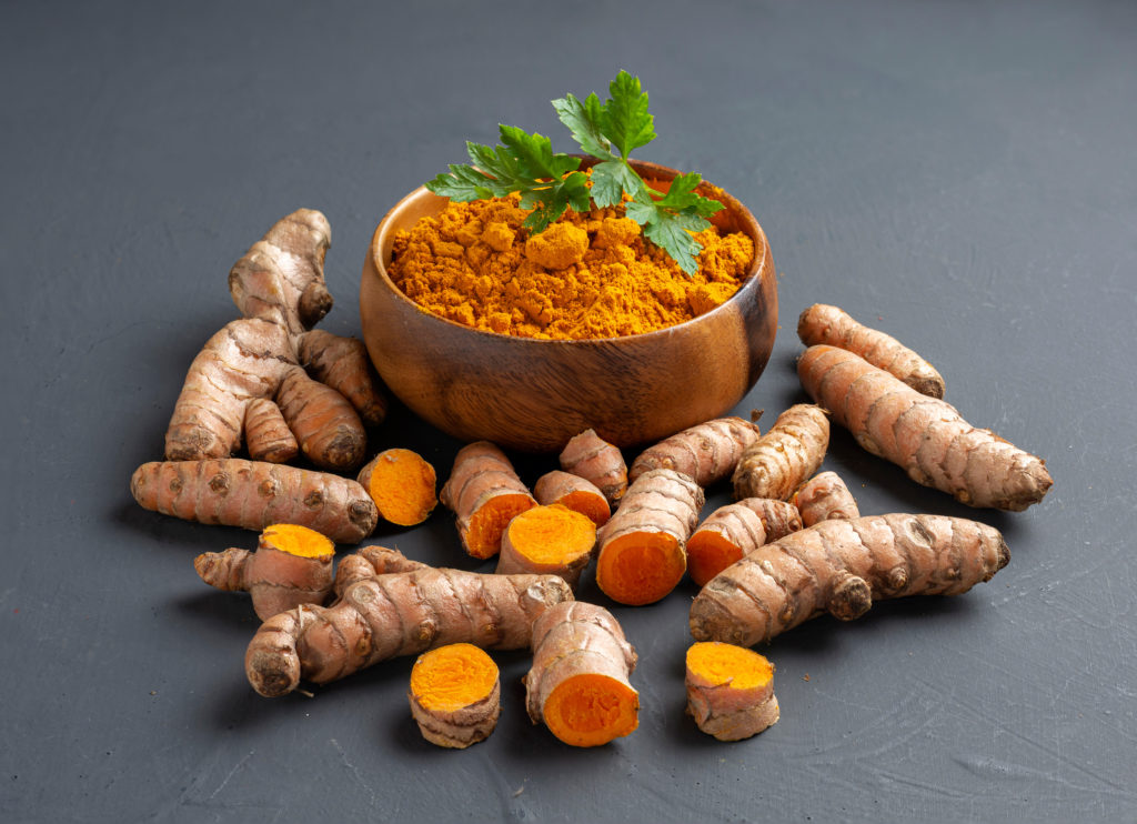 Turmeric powder in a wooden bowl and fresh turmeric on dark background