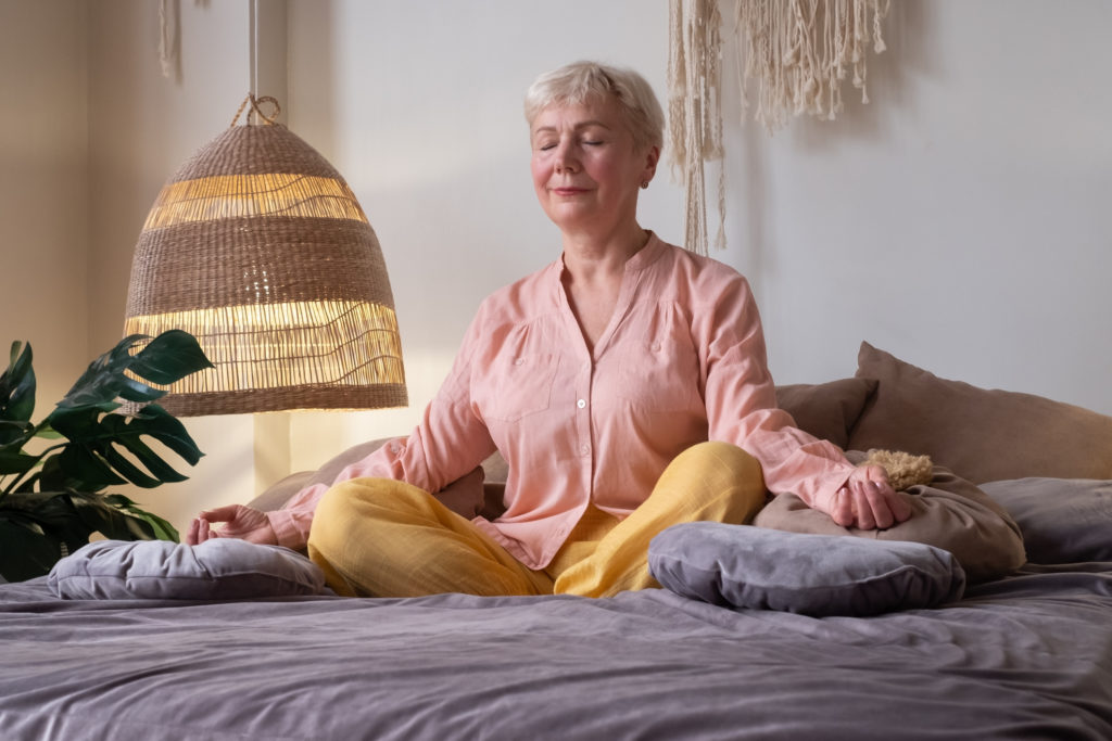 Senior woman meditating practicing yoga indoors. Harmony, yoga practice, balance, meditation, relaxation at home