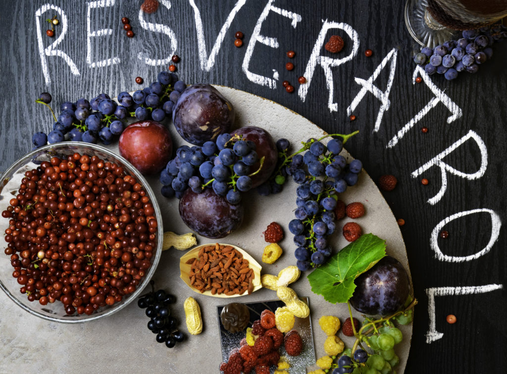 food rich with resveratrol, grapes, plums, goji, peanuts, cranberry,raspberrys dark chocolate, red wine on black wooden background