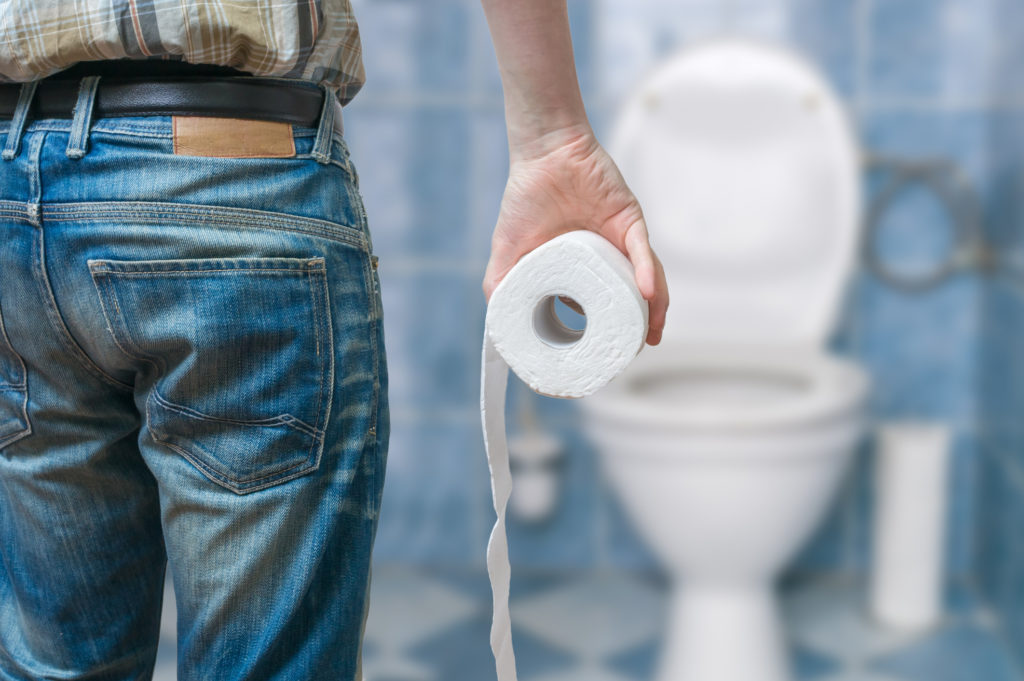 Man suffers from diarrhea or constipation holds toilet paper roll in front of toilet bowl.