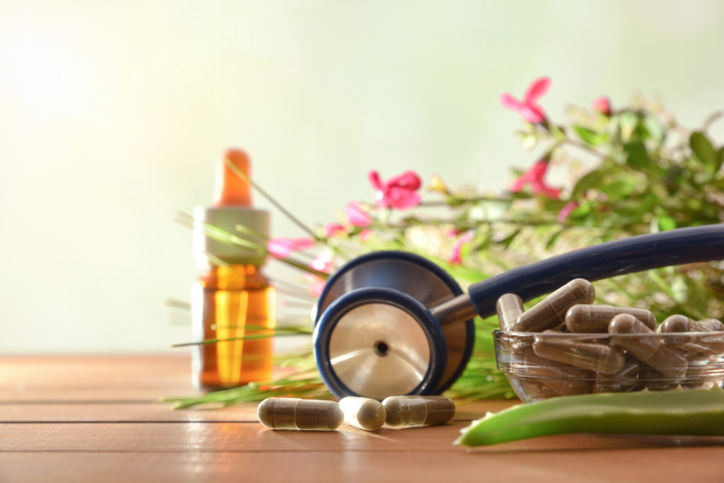 Natural herbal medicine capsules on wood table with stethoscope plants and bottle with medicinal liquid