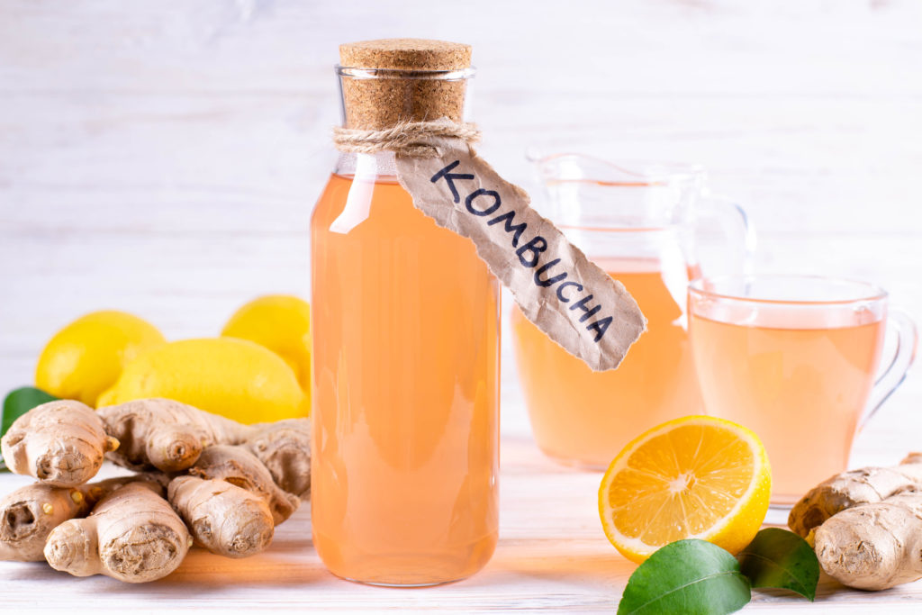 Refreshing filtered kombucha tea in a glass bottle and a glass, with label written kombucha on white wooden background.