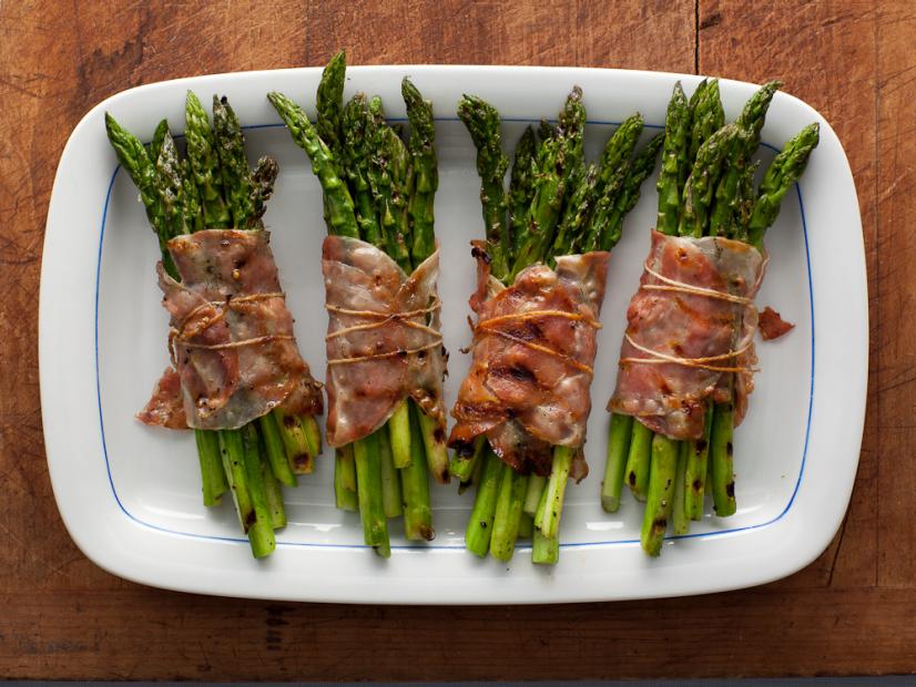 Bacon wrapped asparagus bundles plated on a white platter. 