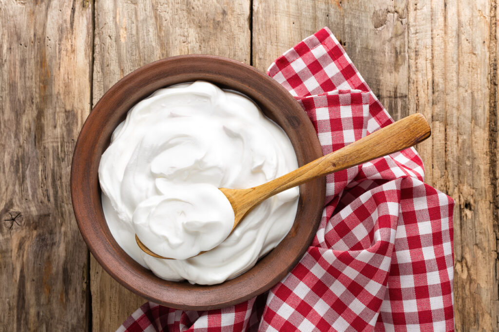Greek yogurt in a brown bowl with wood spoon and checkered napkin 