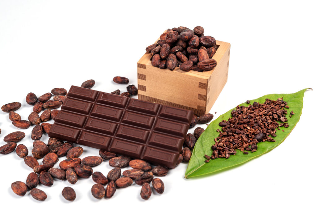 A lot of Cocoa bean in wooden box and pile of cocoa powder on green leaf with chocolate bar isolated on white background