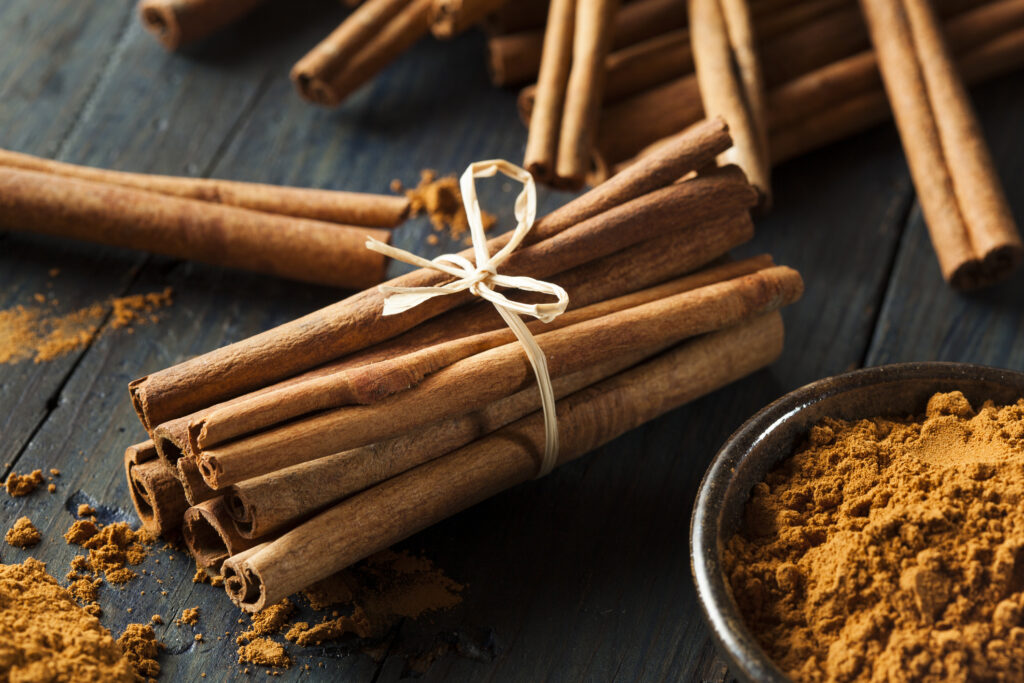 Cinnamon sticks wrapped by string and a bowl of cinnamon powder on a wooden table 