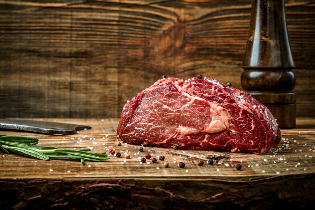 Dry aged Ribeye Steak with seasoning on wooden background. Still life. Copy space. Close-up
