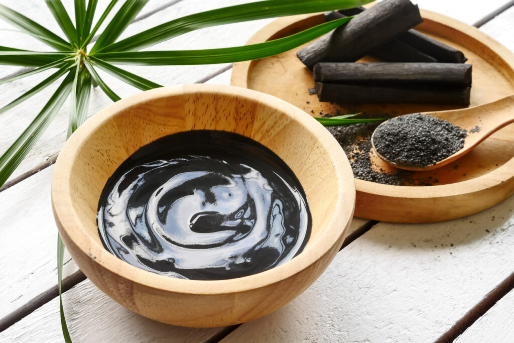 Facial mask and scrub by activated charcoal powder on wooden table cream paste