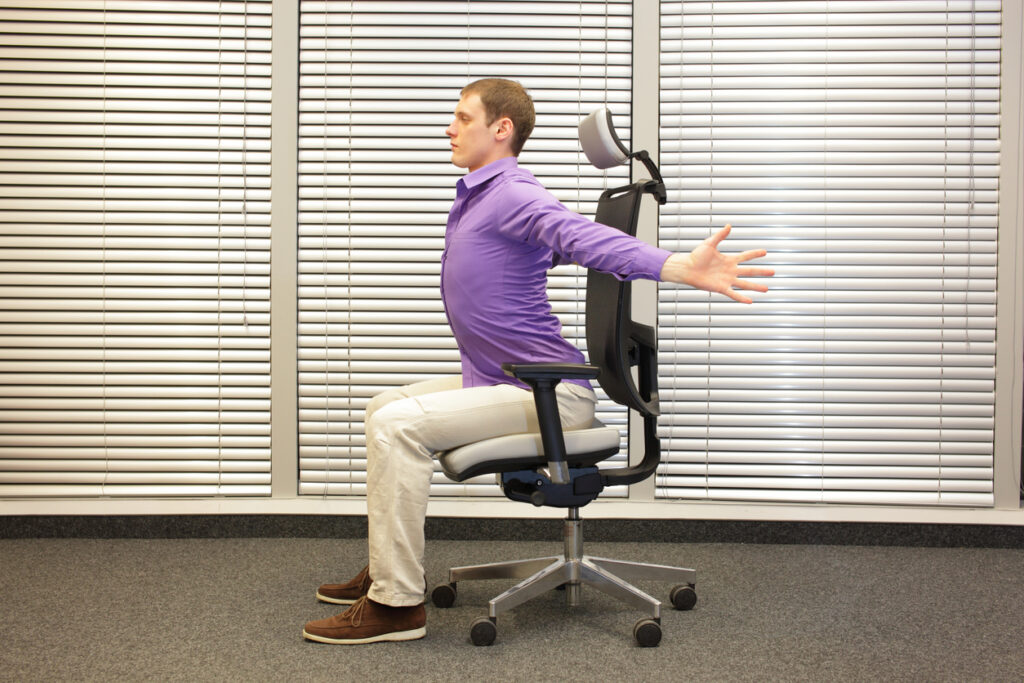 man exercising with his arms out stretched on chair in office, healthy lifestyle - profile view